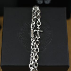 May include: A silver chain bracelet featuring oval links and a central cross charm. The clasp component is engraved with the text .925, indicating the silver purity. The metal has a polished finish with darkened recessed areas for contrast.