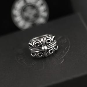 May include: A silver ring featuring an intricate, symmetrical floral-inspired scrollwork design with a central circular accent. The metal has a polished finish with darkened recessed areas to highlight the detailed relief patterns on the band.