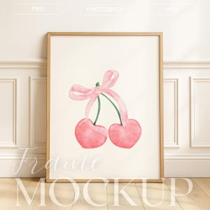 Könnte beinhalten: Ein gerahmter Kunstdruck mit einer Aquarellillustration von zwei rosa Kirschen, die mit einem rosa Band zusammengebunden sind. Das Kunstwerk ist vor einem cremefarbenen Hintergrund platziert und in einem hellbraunen Holzrahmen gerahmt. Unten stehen die Worte "Frame Mockup".