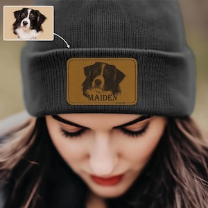 May include: A dark gray beanie with a brown leather patch featuring a dog portrait and the name "MAIDEN". The beanie also has a small image of the dog in the upper left corner.