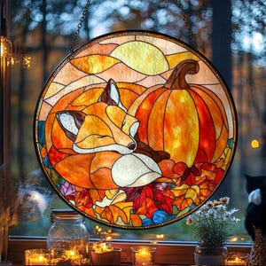 May include: A round stained glass window featuring a sleeping fox next to a large pumpkin. The artwork uses warm colors like orange, yellow, and red, with autumn leaves at the bottom. A chain is attached for hanging.
