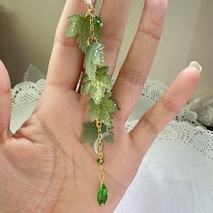 以下が含まれることがあります： 金色のチェーンに、緑色の葉のチャームと緑色のしずく型のクリスタルペンダントが付いています。半透明の葉はさまざまな緑色をしています。透明と緑のクリスタルビーズもチェーンに取り付けられています。