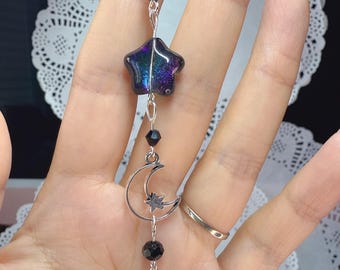 May include: A celestial-themed charm featuring a star, moon, and teardrop pendant. The star is iridescent with purple and blue hues. The moon and star are silver-toned, and the teardrop is a faceted, dark gray crystal. Black beads connect the elements.
