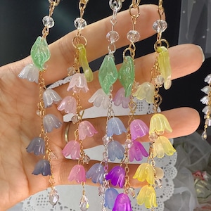 May include: A collection of colorful, floral-themed accessories. Each piece features delicate, translucent flower and leaf charms in shades of white, pink, blue, purple, and yellow, strung on gold-tone and silver-tone chains with crystal accents.
