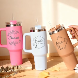 May include: Three personalized insulated tumblers with handles and straws. One is pink with "Naomi" and a floral design, another is white with "Camila 06.15.2025", and the third is tan with "Rafael".