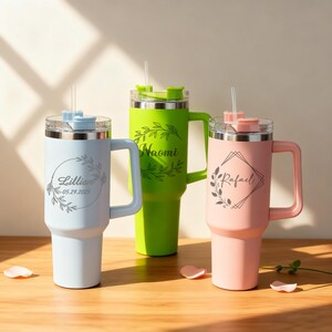 May include: Three personalized tumblers in pastel colors: light blue, green, and pink. Each tumbler has a handle, a clear lid, and a straw. The light blue tumbler has the name "Lillian" and the date "05.29.2025". The green tumbler has the name "Naomi". The pink tumbler has the name "Rafael".