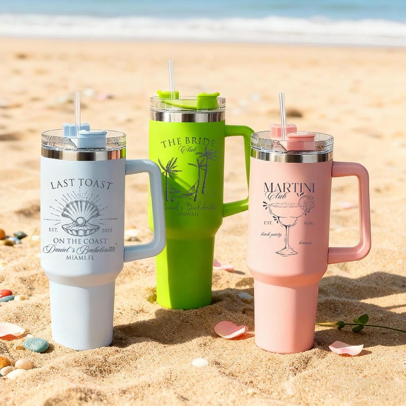 Pu&ograve; includere: Tre bicchieri isolanti con manici e cannucce su una spiaggia sabbiosa. I bicchieri sono azzurri, verdi e rosa. Ognuno ha un design e un testo diverso: "Last Toast", "The Bride Club" e "Martini Club".