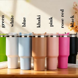 Pu&ograve; includere: Una collezione di bicchieri isolanti in vari colori, tra cui verde, bianco, blu, kaki, rosa, rosso rosa e nero. Ogni bicchiere ha un coperchio trasparente e un bordo in acciaio inossidabile. I colori sono etichettati.