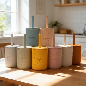 May include: A collection of eight colorful, personalized sippy cups with lids and straws. Each cup is a different pastel color, including blue, yellow, pink, and beige. The names "Olivia", "Violet", "Sophia", "Isabella", "Mateo", and "Harper" are printed on the cups.