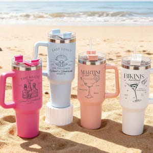 Pu&ograve; includere: Quattro bicchieri isolati con manici e cannucce su una spiaggia sabbiosa. I bicchieri sono rosa, azzurro, pesca e bianchi. Ogni bicchiere ha un design e un testo diverso, tra cui "The Bride Club", "Last Toast", "Martini Club" e "Bikinis + Martinis".
