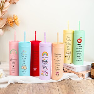 May include: A collection of personalized tumblers with straws in various colors, including pink, blue, red, purple, yellow, and green. Each tumbler features custom text and graphics, such as rainbows, flowers, and the text "Thank you".