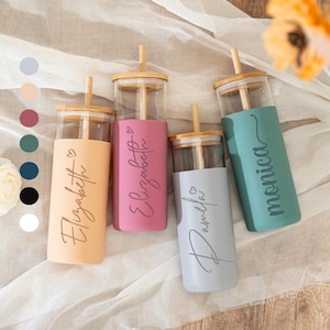 May include: Four glass tumblers with bamboo lids and straws. Each tumbler has a colored silicone sleeve with a name in cursive script: Elizabeth, Elizabeth, Pamela, and Monica. The colors are peach, pink, gray, and teal.