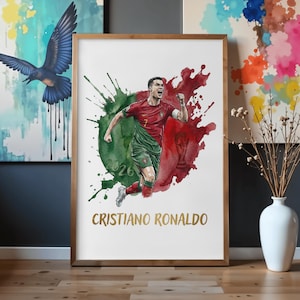 Watercolor style sports poster featuring Cristiano Ronaldo celebrating in a red and green Portugal football kit. The background shows abstract green and red paint splatters mimicking the Portuguese flag, with a subtle World Cup trophy silhouette and the year 2026. The name "CRISTIANO RONALDO" is printed in an elegant gold font at the bottom. The print is showcased in a light wood frame resting on a floor.