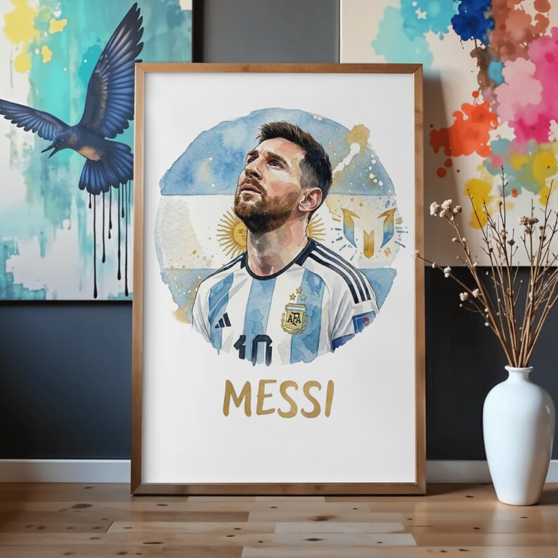 Watercolor portrait poster of Lionel Messi looking upward, wearing the classic blue and white striped Argentina football jersey with the AFA logo and three stars. The background features a circular abstract watercolor design of the Argentine flag with the Sun of May and his signature logo. The name "MESSI" is written in gold text below the artwork. The poster is displayed in a light wooden frame.