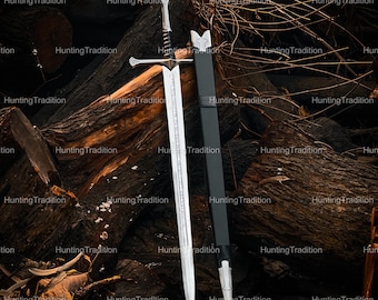 May include: A silver sword with a decorative hilt and a black sheath. The sword's blade is long and sharp, with intricate detailing. The sheath is made of black leather. The sword is displayed against a backdrop of wooden logs.