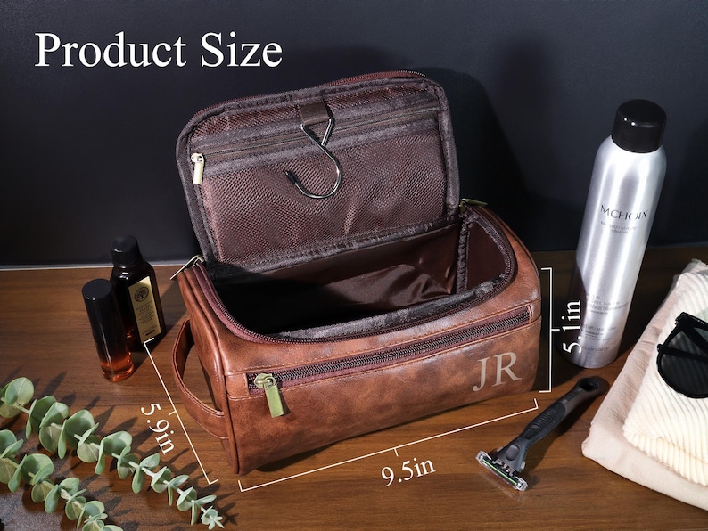 Op de afbeelding: Bruin leren toilettas met ritssluiting, 24 cm lang, 15 cm breed en 13 cm hoog. De tas is open en toont een bruin interieur. De initialen "JR" zijn zichtbaar aan de zijkant. Andere items zijn zichtbaar.