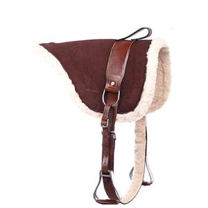 Puede incluir: Una silla de montar de caballo de ante marrón con forro de vellón color crema. La silla tiene correas de cuero, estribos y un asa. El equipo ecuestre está diseñado para la comodidad y el control.
