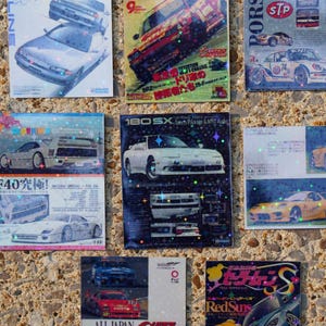 Op de afbeelding: Een verzameling van negen vintage tijdschriftknipsels en promokaarten met autothema. De afbeeldingen tonen verschillende automodellen, waaronder Porsches en Japanse sportwagens, met Japanse tekst en levendige kleuren. Het algemene thema is automotive.