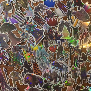 May include: A collection of holographic stickers featuring various fantasy characters and creatures. The stickers have a shiny, iridescent finish and are in various shapes and sizes. The designs include warriors, monsters, and other fantastical elements.