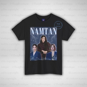 May include: Black t-shirt featuring a graphic of three women with the word "NAMTAN" above them. The graphic has a vintage aesthetic with a lightning bolt background. The shirt has a crew neck.