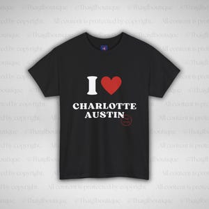 May include: Black t-shirt featuring the text "I ❤️ CHARLOTTE AUSTIN" in white with a red heart symbol. The shirt has a crew neck and short sleeves. The text is centrally positioned on the front of the garment.