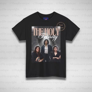 Może przedstawiać: Czarny t-shirt z napisem "THE HOLY Trinity" nad zdjęciem trzech kobiet. Obraz ma miękką, eteryczną jakość. Koszulka ma okrągły dekolt i krótkie rękawy.