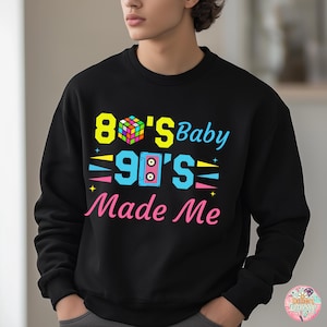 May include: Black sweatshirt with the text "80's Baby 90's Made Me" in bright colors. The design includes a Rubik's Cube, a boombox, and stars. The sweatshirt is a crew neck style.