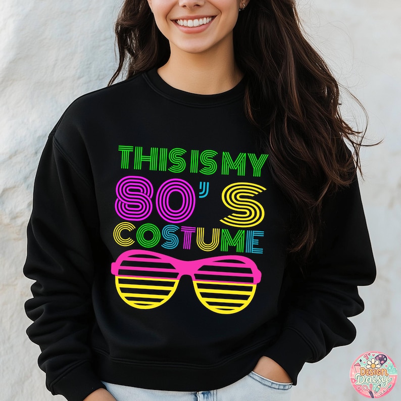 May include: Black sweatshirt with the text "THIS IS MY 80'S COSTUME" in neon green, purple, yellow, and blue. The design includes a pair of pink and yellow shutter shades. The sweatshirt is a retro-themed costume.