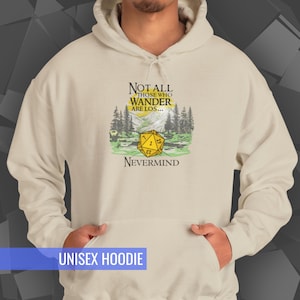 May include: A cream-colored unisex hoodie featuring a graphic with the text "NOT ALL THOSE WHO WANDER ARE LOS... NEVERMIND." The graphic includes a yellow 20-sided die, mountains, and trees. The bottom of the hoodie reads "UNISEX HOODIE."