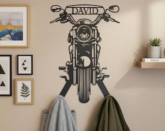 May include: Black metal motorcycle-shaped wall art with the name "DAVID" above the handlebars. The art piece functions as a coat rack, with two hooks below the motorcycle. A gray jacket and an olive green jacket hang from the hooks.
