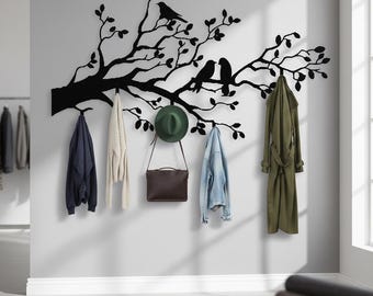 Puede incluir: Un perchero de pared de metal negro con forma de rama de árbol con dos pájaros posados. Varios abrigos, un sombrero y un bolso cuelgan de los ganchos. Los abrigos son azul marino, crema, vaquero y verde oliva.