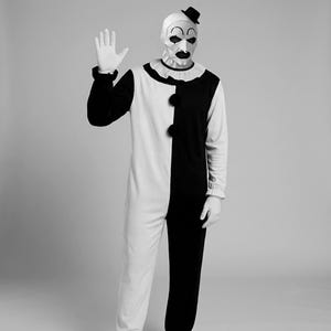 Peut inclure: Un costume de clown noir et blanc composé d'une combinaison à manches longues avec un design bicolore, un col à volants et deux gros pompons noirs sur la poitrine. L'ensemble comprend un masque blanc aux traits noirs et un petit chapeau haut-de-forme.