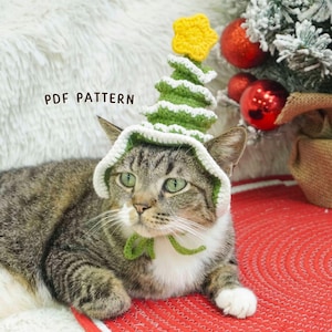 Könnte beinhalten: Eine getigerte Katze trägt einen handgefertigten Häkel-Weihnachtsbaumhut mit einem gelben Stern. Die Katze liegt auf einer roten Matte, mit einem Weihnachtsbaum und Kugeln im Hintergrund. Der Text "PDF PATTERN" ist sichtbar.