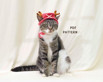 May include: A tabby cat wearing a red crocheted hat with brown antlers and a matching red collar. The cat is sitting and looking at the camera. The text "PDF PATTERN" is visible in the background.