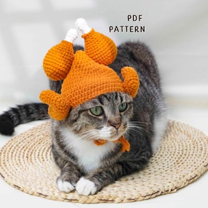 May include: A tabby cat wearing a handmade orange crochet turkey hat and matching neck piece. The hat features drumstick and turkey head details. The cat is sitting on a woven mat. The text "PDF PATTERN" is visible.
