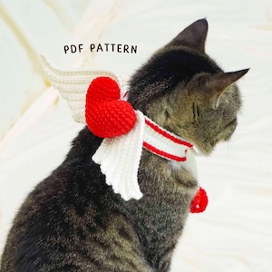May include: A tabby cat wearing a crocheted angel wing and heart collar. The wings are white, and the heart is red. The collar has red and white stripes. The text "PDF PATTERN" is visible.
