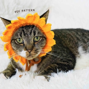 Könnte beinhalten: Eine getigerte Katze mit einem hellorangefarbenen gehäkelten Sonnenblumenhut. Die Katze liegt auf einer flauschigen, weißen Oberfläche. Der Text "PDF PATTERN" befindet sich über dem Kopf der Katze.