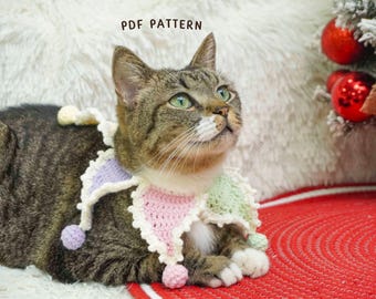 May include: A tabby cat wearing a colorful, crocheted collar with a jester-like design. The collar features pastel pink, green, and lavender sections with small pom-poms. The text "PDF PATTERN" is visible. The cat is on a white fluffy surface.