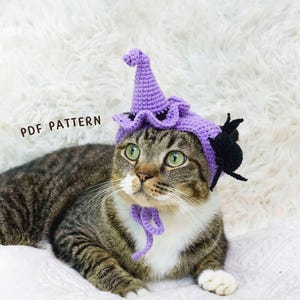 Puede incluir: Un gato atigrado con un sombrero de bruja morado tejido a ganchillo con un acento de araña negra. El sombrero tiene un borde con volantes y una parte superior puntiaguda. El gato está tumbado sobre una superficie blanca y esponjosa. El texto de la imagen dice "PDF PATTERN".