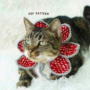 May include: A tabby cat wearing a crocheted Demogorgon flower collar. The collar is red with white spots and gray trim. The text "PDF PATTERN" is visible in the image.