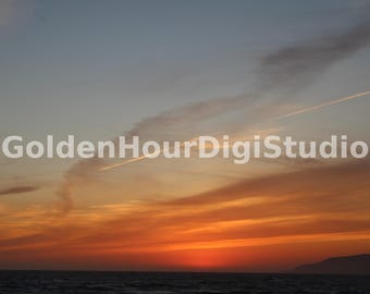 May include: A vibrant sunset sky with streaks of orange, pink, and yellow clouds. The horizon is a deep blue, and the sky is filled with wispy clouds.