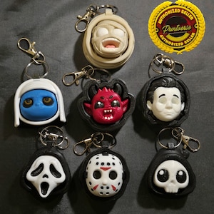 May include: Collection of horror-themed keychains featuring various characters. Includes a mummy, a blue-skinned figure, a devil, a classic horror movie character, a ghost face, a hockey mask, and a skull. Each keychain has a silver clasp.