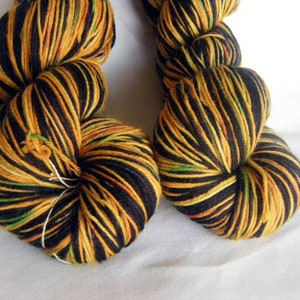 May include: Two skeins of yarn in a black, orange, yellow, and green colorway. The yarn is striped and has a hand-dyed look.