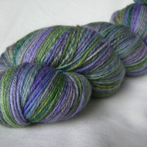 May include: A skein of hand-dyed yarn in shades of green, purple, and blue. The yarn is tightly wound and appears soft, with subtle variations in color throughout. Ideal for knitting or crochet projects.