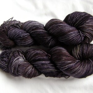 Peut inclure: Deux &eacute;cheveaux de fil de couleur violet fonc&eacute; avec un motif de couleur vari&eacute;. Le fil est torsad&eacute; et boucl&eacute;, montrant la texture et les variations de couleur.