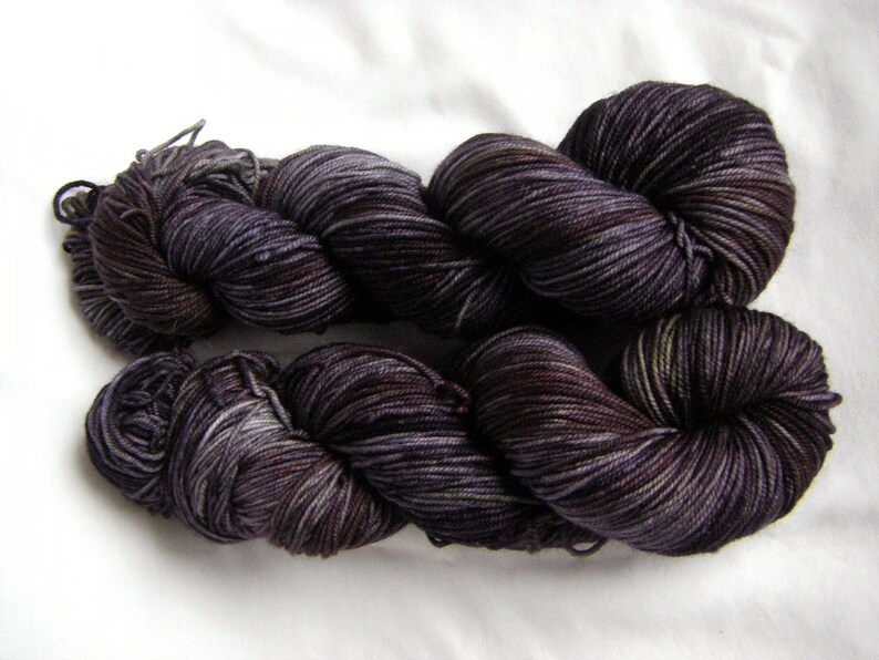 Peut inclure: Deux &eacute;cheveaux de fil de couleur violet fonc&eacute; avec un motif de couleur vari&eacute;. Le fil est torsad&eacute; et boucl&eacute;, montrant la texture et les variations de couleur.