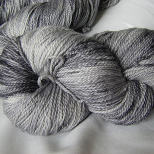 May include: A skein of yarn in a variegated gray and black colorway. The yarn is soft and fluffy, and it is perfect for knitting or crocheting.