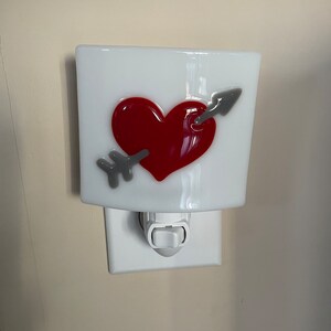 May include: White ceramic nightlight with a red heart pierced by a gray arrow. The nightlight has a white on/off switch.