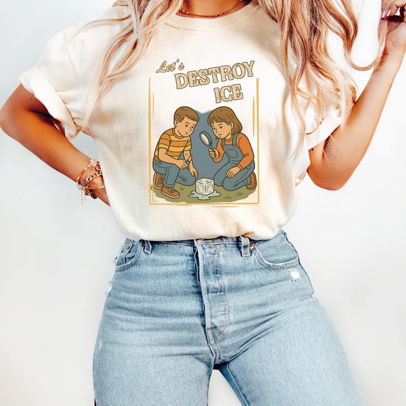 May include: Cream-colored t-shirt featuring a retro illustration of two children examining a cube of ice with a magnifying glass. The text "Let's DESTROY ICE" is above the illustration. The children are wearing overalls and a striped shirt.