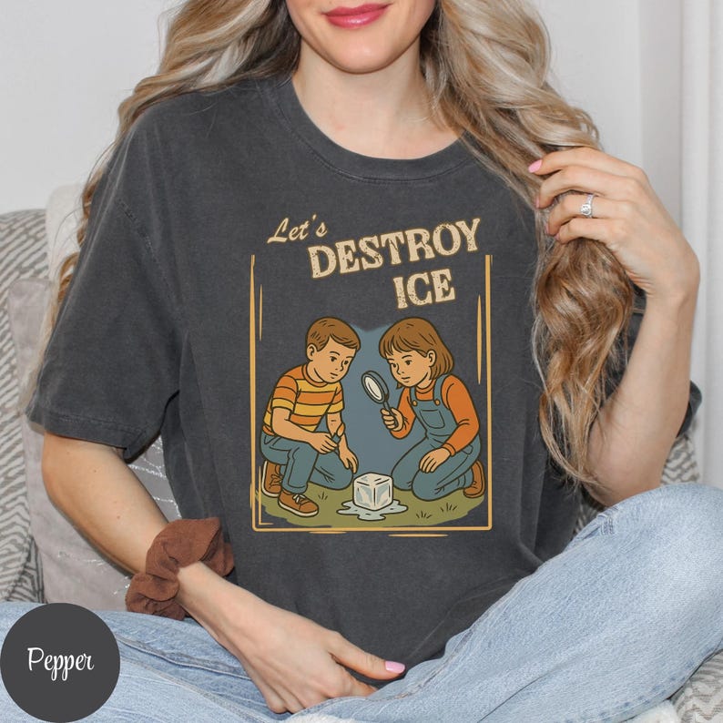 May include: Dark gray t-shirt with the text "Let's DESTROY ICE" above an illustration of two children examining a melting ice cube with a magnifying glass. The children are wearing orange and blue clothing.